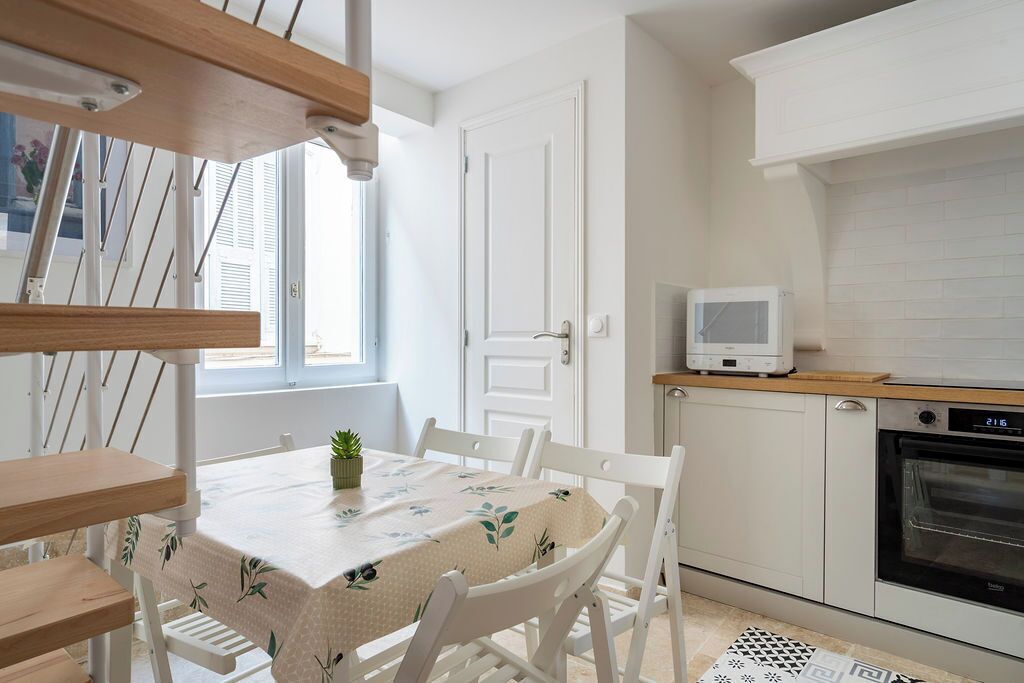 Une cuisine compacte avec des meubles blancs, un four encastré et un petit téléviseur posé sur une étagère en bois.
