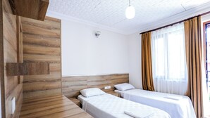 Ein Hotelzimmer mit zwei Einzelbetten, einem Holz-Kopfteil, weißen Wänden und einem Fenster mit Vorhängen.