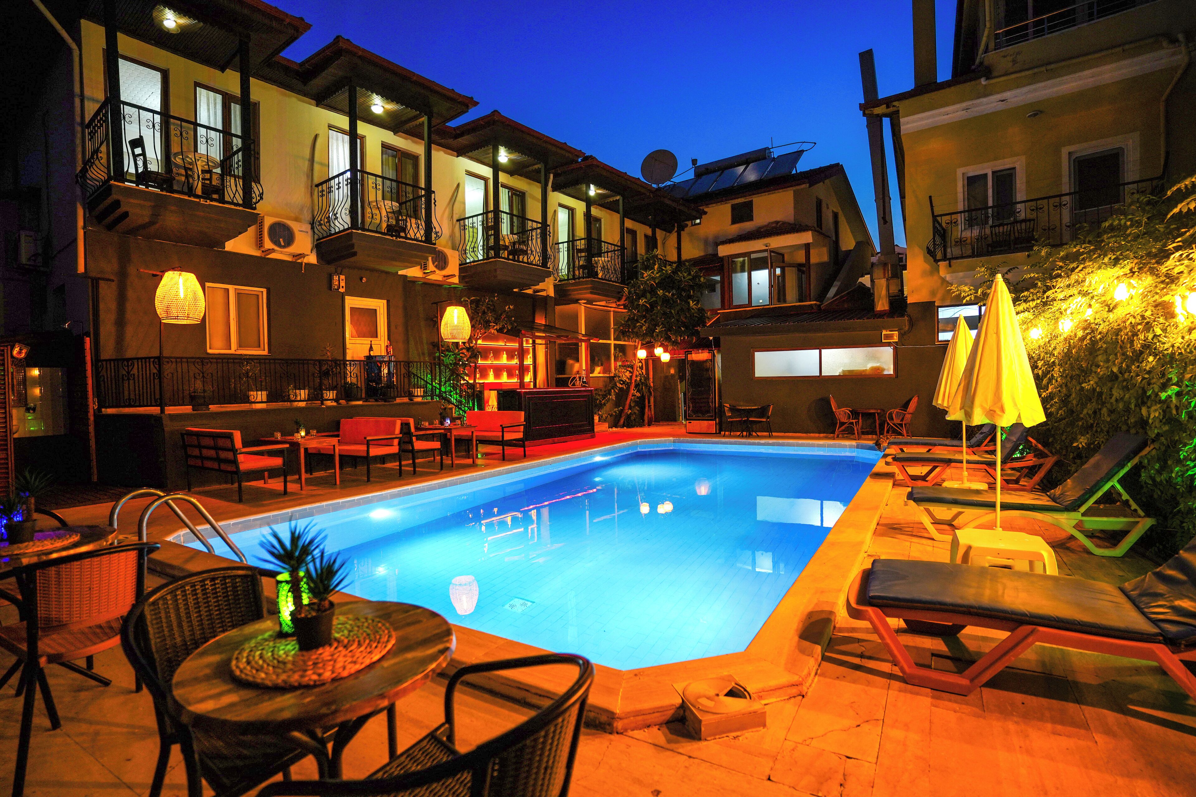 A swimming pool with lounge chairs and tables, surrounded by buildings with balconies and outdoor seating.