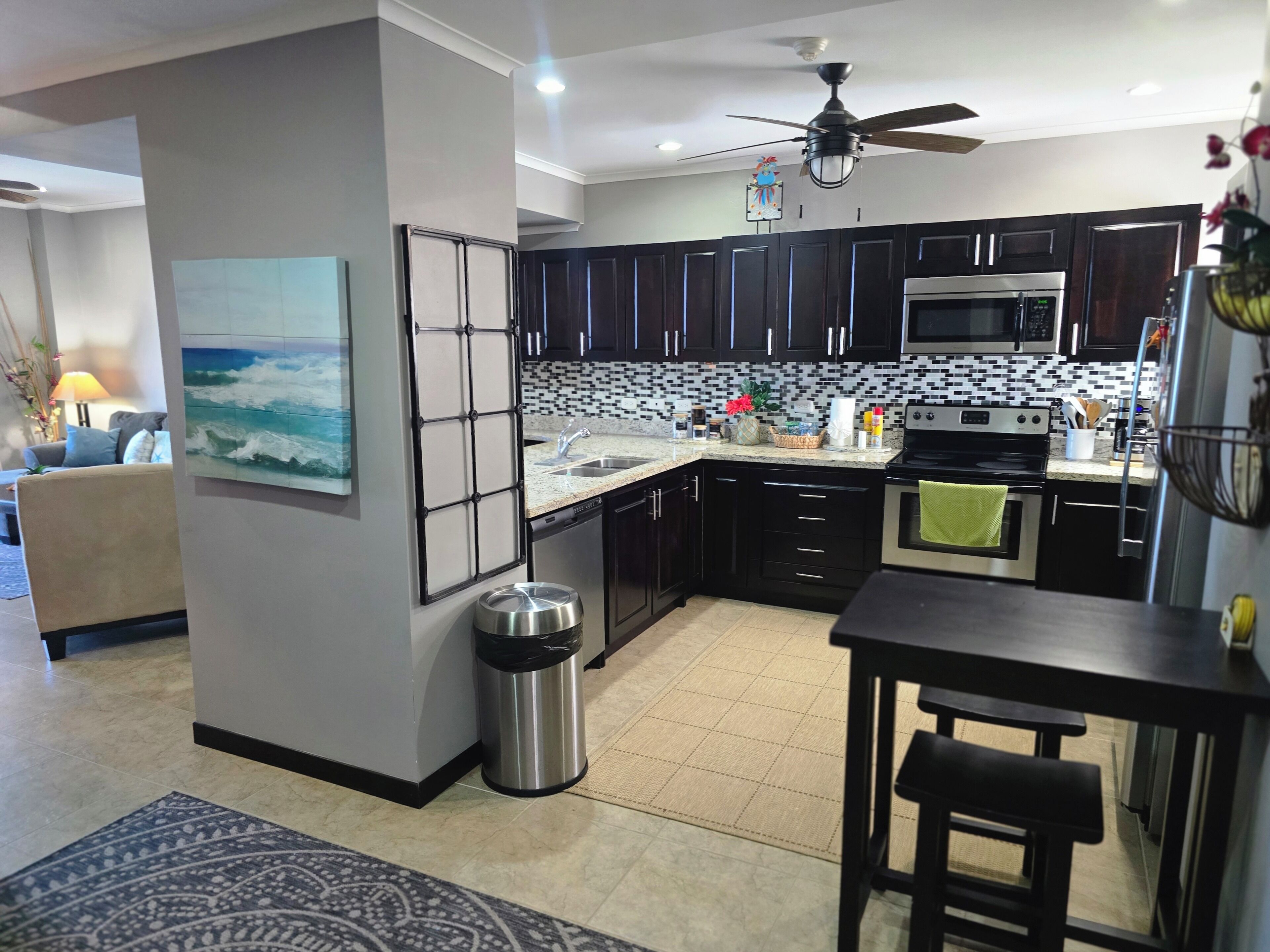 A modern kitchen with dark cabinetry, a microwave, an oven, and a ceiling fan.