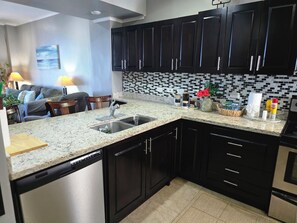 A kitchen with dark cabinets, a granite countertop, a dishwasher, and a tiled backsplash. - Apartment by the Sea • Balcony with a view of the sunset - Access to the Crocs Resort - Direct beach access - (Jaco)