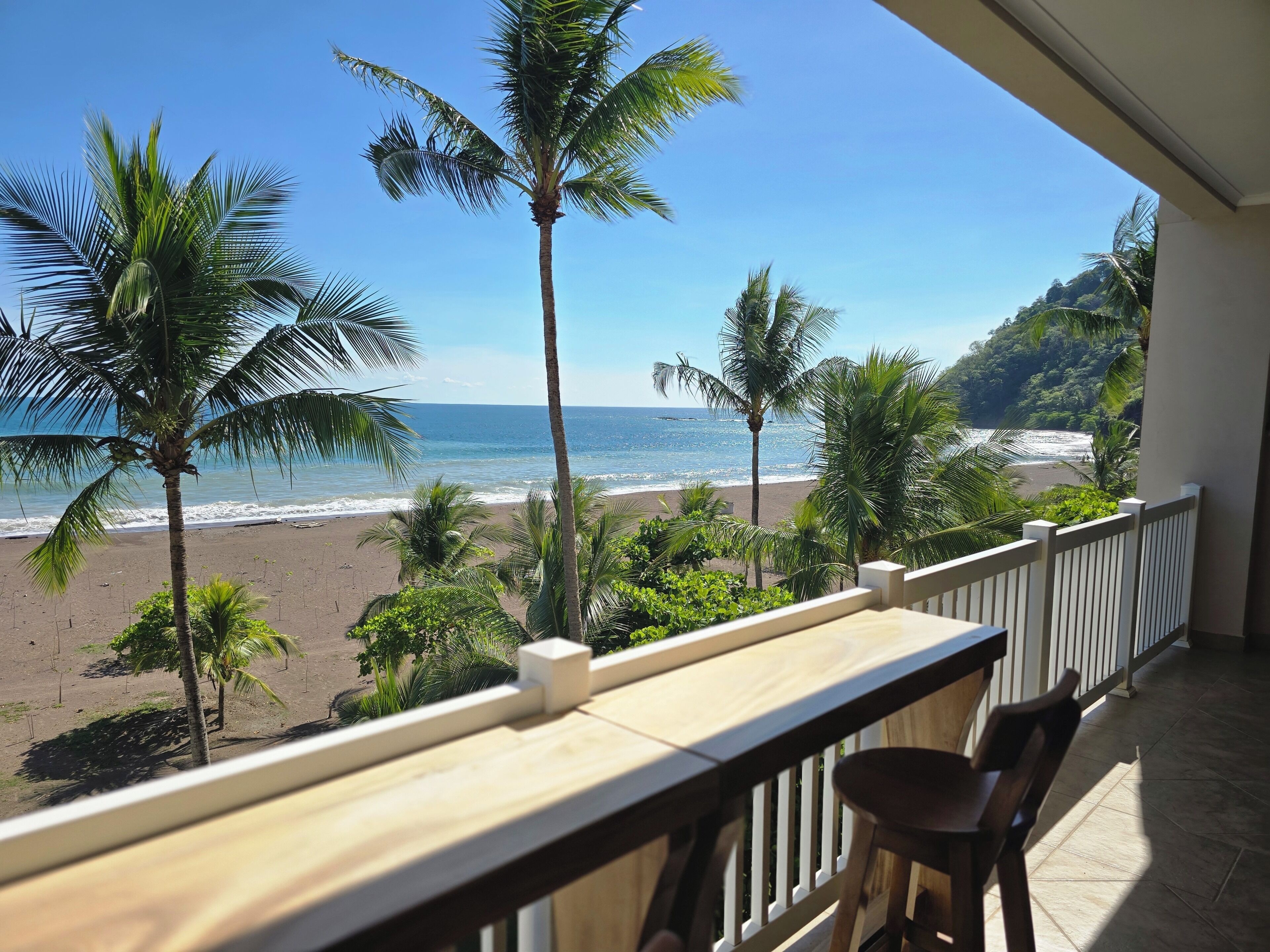 A balcony with a view of a beach, palm trees, and a mountainous landscape.