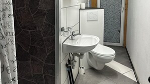 Moderni kylpyhuone, jossa on kivipintainen suihkuseinä, valkoinen pesuallas ja wc.