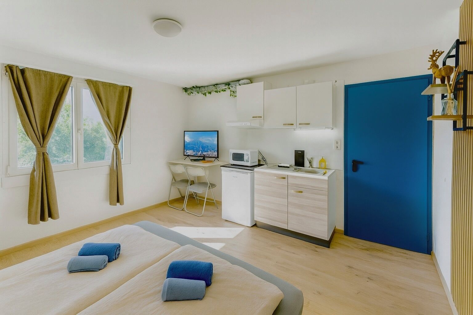 Une petite pièce comprenant un lit, un bureau, un coin cuisine et une porte bleue.