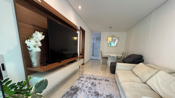 A modern living room with a flat-screen TV mounted on a wooden panel, a beige sofa, a gray shag rug, and a dining area with a white table and chairs. - Quiet house - close to Vitória airport (Vitória)
