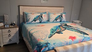 Une chambre à coucher avec un lit en bois, une tête de lit et un pied de lit assortis. On y trouve une table de chevet avec une horloge et une petite lampe. Un tableau mural avec l'inscription « Je t'aime plus que tout » est visible.