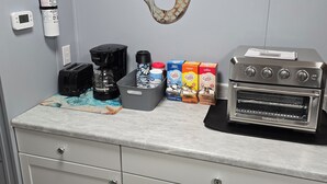Un comptoir de cuisine avec une machine à café, un grille-pain et des dosettes de café. Un extincteur et un détecteur de fumée sont fixés au mur.
