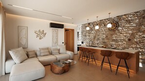 Een moderne woonkamer met een bank, een salontafel en een keukenhoek met een stenen muur en barstoelen.