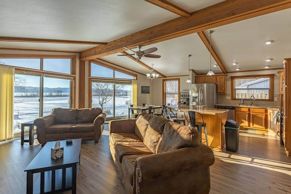 A spacious living area with a large sofa set, a dining table, and a kitchen with wooden cabinets and a refrigerator.