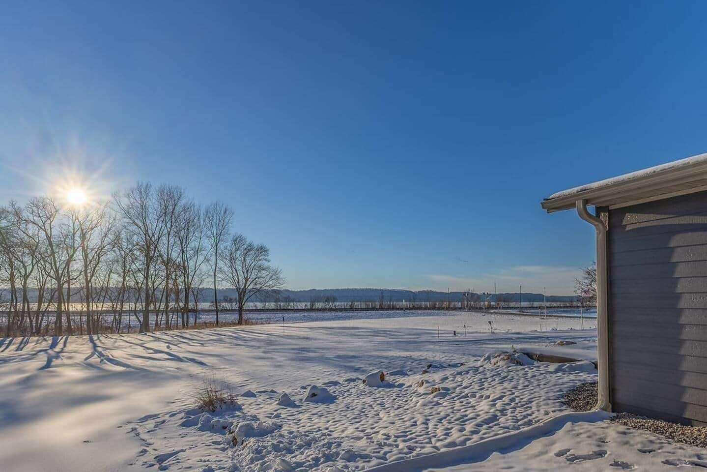 Un espace extérieur enneigé, avec un bâtiment sur la droite, un ciel dégagé et une vue lointaine d’un pont.