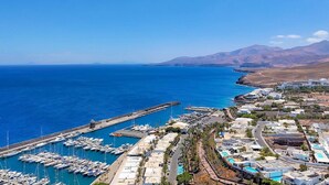 A coastal marina with numerous boats docked, a pier extending into the sea, and a residential area with buildings and roads. - Villa Puerto Calero Marina | Short Walk to Centre | Private Heated Pool (Lanzarote)