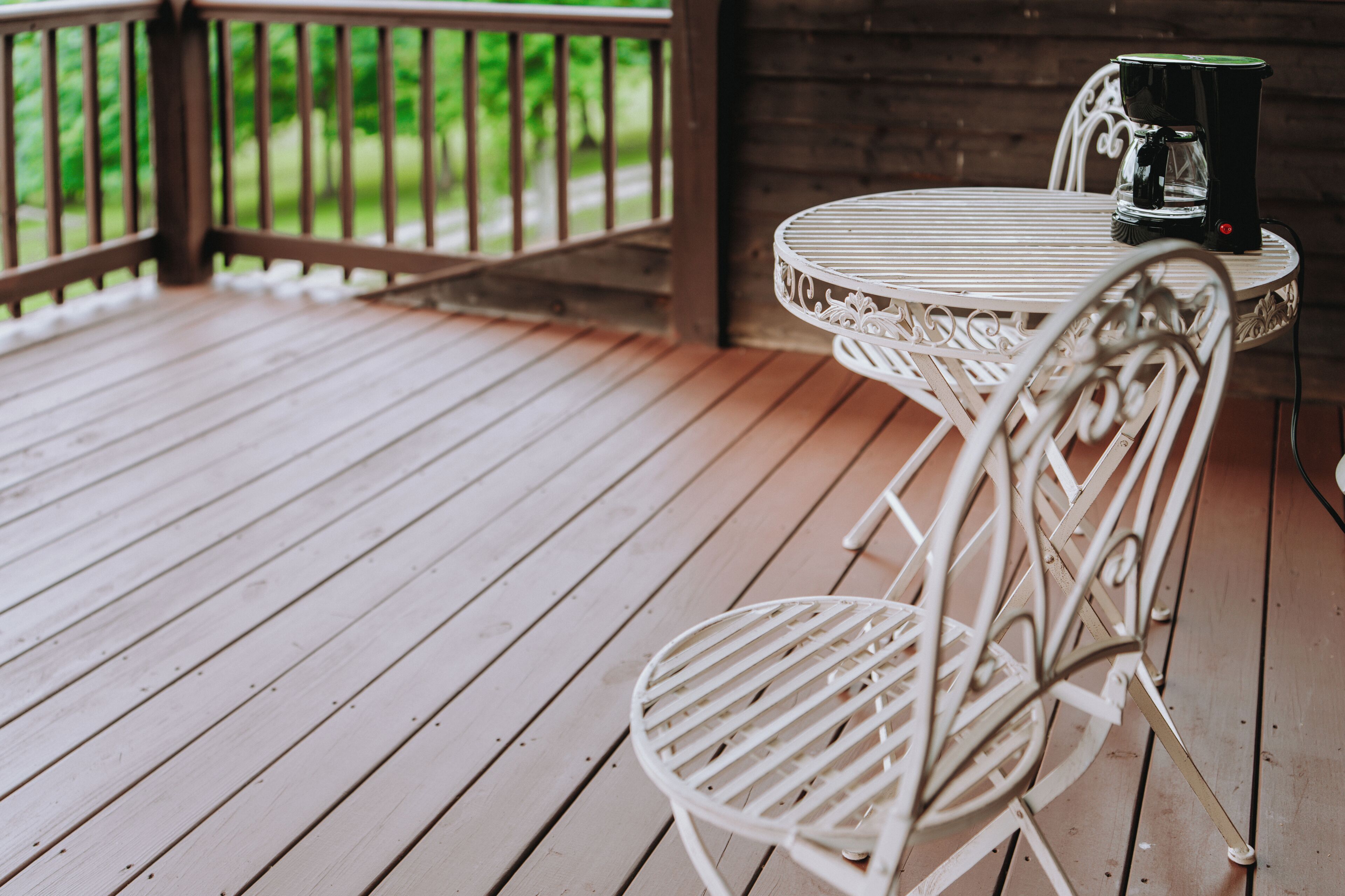 A white metal table and chair set on a wooden deck with a coffee maker on the table.