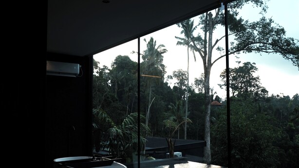 Une chambre moderne dotée d’une grande fenêtre donnant sur une piscine et une végétation luxuriante.