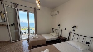 Hotellihuone, jossa on kaksi sänkyä, liukuovella varustettu lasiterassi, ilmastointilaite ja pieni pöytä.