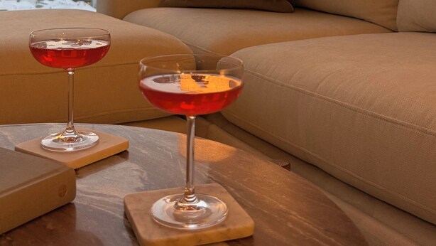 Una sala de estar moderna con un sofá, dos bebidas sobre posavasos, una lámpara y vistas a la ciudad a través de una ventana.