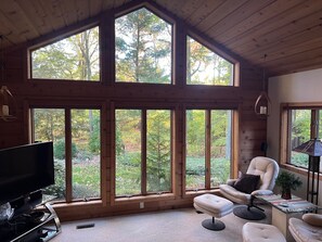 A spacious room with large windows, a comfortable chair, a small ottoman, and a television. - The Scandinavian Chalet - Tranquility in Town (Midland)