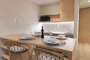 A dining area with a table set for four, including wine glasses and a bottle of wine. There are wicker chairs and a modern kitchen in the background. - 205 Fabulous Apt near La Diana/Reforma/U.S Embassy (Mexico City)