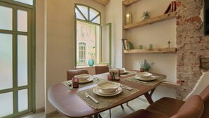 Un comedor con una mesa de madera dispuesta para cuatro personas, rodeada de sillas de cuero marrón. Se observan una pared de ladrillo y estanterías de madera con objetos decorativos al fondo.