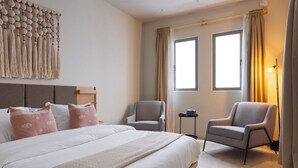 Ett hotellrum med en stor säng, två fåtöljer, ett litet bord och en dekorativ tavla som hänger på väggen.