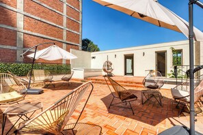 Eine Außenpatio mit Korbstühlen, einem weißen Sonnenschirm, einer Ziegelmauer und einem Gebäudeeingang.