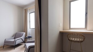 Et moderne værelse med en grå sofa, en fletstol, et lille bord med pynteting og et vindue med gardiner.