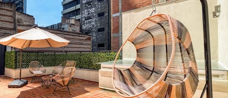 Eine Dachterrasse mit Korbstühlen, einer Hängematte und einem Tisch unter einem großen Sonnenschirm.