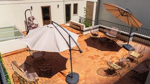 Eine Dachterrasse mit Sitzgelegenheiten im Freien, einem großen Sonnenschirm und einem Geländer aus Glas.