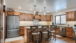A kitchen with wooden cabinets, a stainless steel refrigerator, a central island with chairs, and pendant lighting. - Sturgis Motorcycle Rally Rental - 5 bedroom with garage (Spearfish)