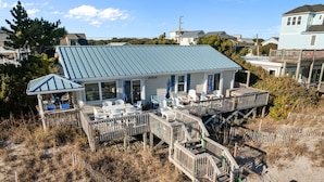Ein Küstenhaus mit blauem Dach, einer Terrasse mit Gartenmöbeln und einem Strandabschnitt.