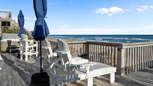 Eine Holzterrasse mit weißen Liegestühlen und blauen Sonnenschirmen mit Blick aufs Meer.