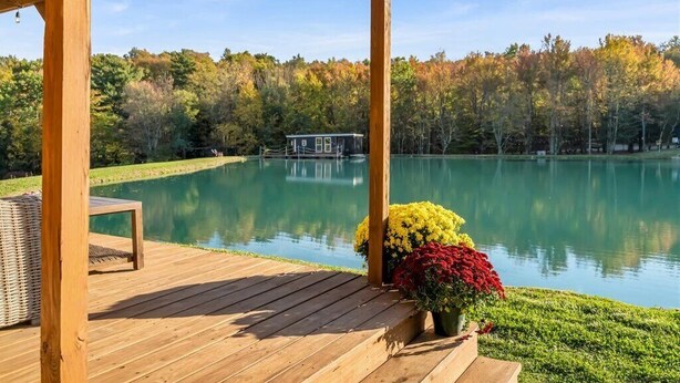 A wooden deck with a gazebo, a pond, and autumn-colored trees in the background.