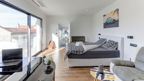 Et moderne soveværelse med seng, sofa, en bærbar computer på et skrivebord og et billede på væggen.