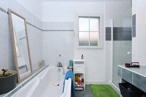 A bathroom with a bathtub, a mirror, a window, and a sink area. - L'écrin sous les chênes - Wifi - Jardin (Olivet)