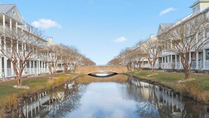 Un canal surmonté d’un pont de pierre, bordé de bâtiments aux façades blanches et aux colonnes symétriques, dont le reflet se mire dans l’eau.