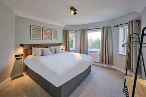 Ein modernes Hotelzimmer mit einem großen Bett, einem Nachttisch, einer Wandlampe und einem Fenster mit Vorhängen.