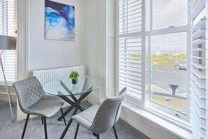 A modern room with a glass table, two grey chairs, a radiator, and a large window with blinds. - Host Stay The Langle Hotel Apartment 1 (Whitby)