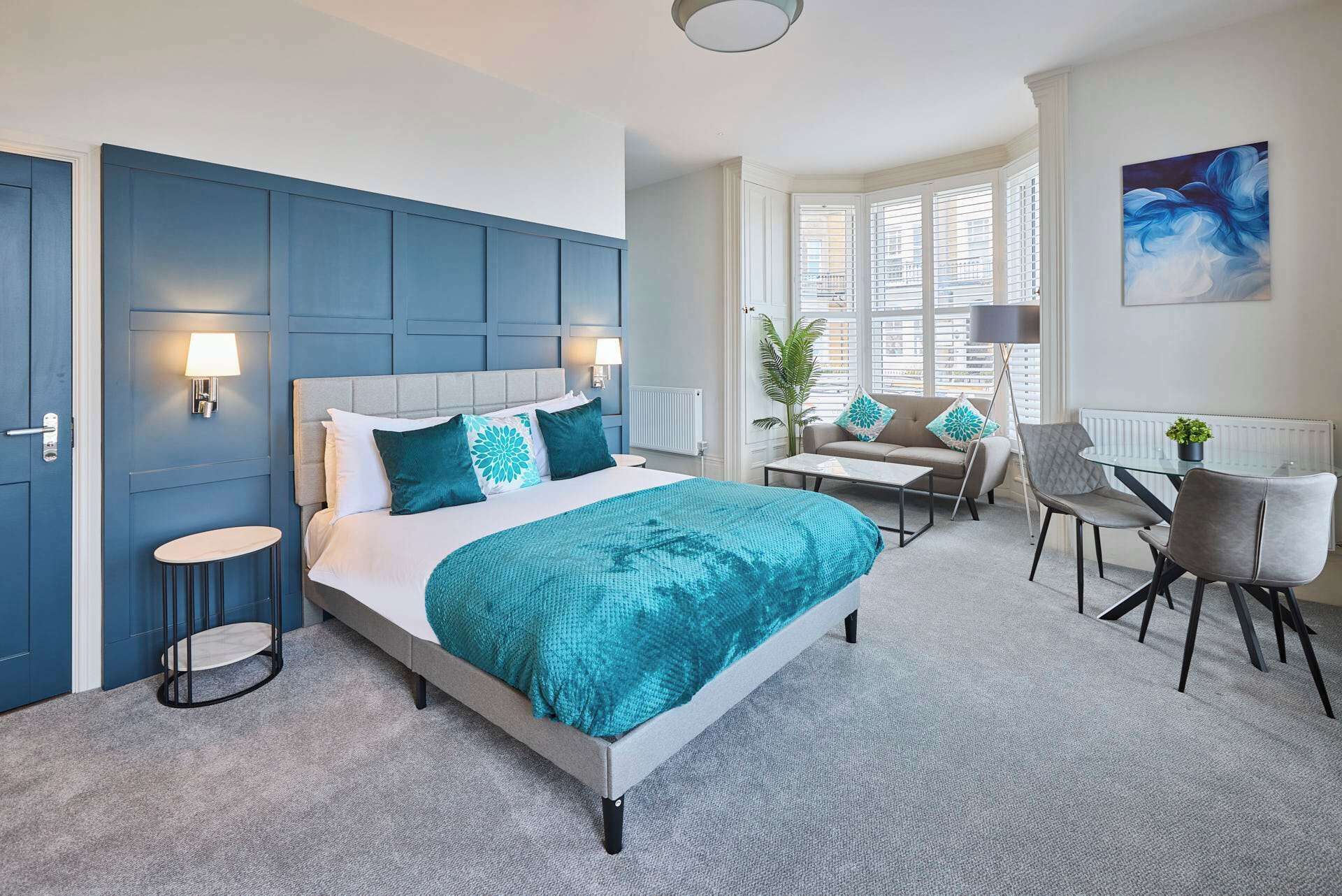 A modern bedroom with a large bed, bedside tables, a desk, and a window with blinds.