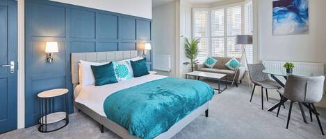 A modern bedroom with a large bed, bedside tables, a desk, and a window with blinds.
