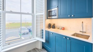 Una cocina con armarios azules, un microondas, un fregadero y una ventana con vista a un estacionamiento.