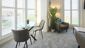 Un salon moderne avec une table en verre, deux fauteuils, un canapé et une grande plante en pot.