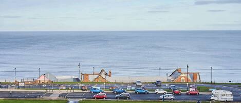 A coastal parking area with vehicles, a pedestrian walkway, and a view of the sea.