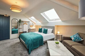 Een moderne slaapkamer met dakraam, een bed met blauwgroene beddengoed, een bank en een bijzettafeltje.