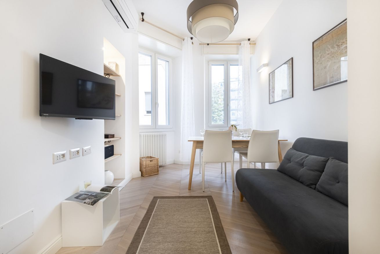 Un salon moderne doté d’un téléviseur à écran plat, d’un canapé, d’une table à manger avec des chaises et d’une grande fenêtre laissant entrer la lumière naturelle.
