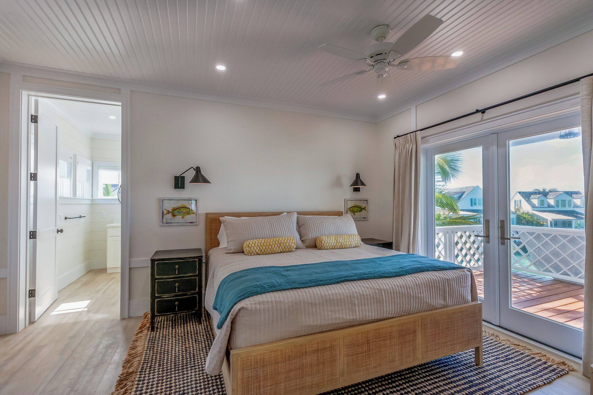 A bedroom with a bed, bedside tables, a ceiling fan, and a view of the outside.