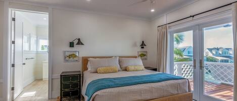 A bedroom with a bed, bedside tables, a ceiling fan, and a view of the outside.