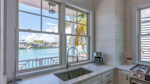 A kitchen with a view of a marina, a sink, a coffee maker, and a stove. - 1 Bedroom Villa - Sunset Point, Abaco -SeaScape Villa # 9 (Elbow cay)