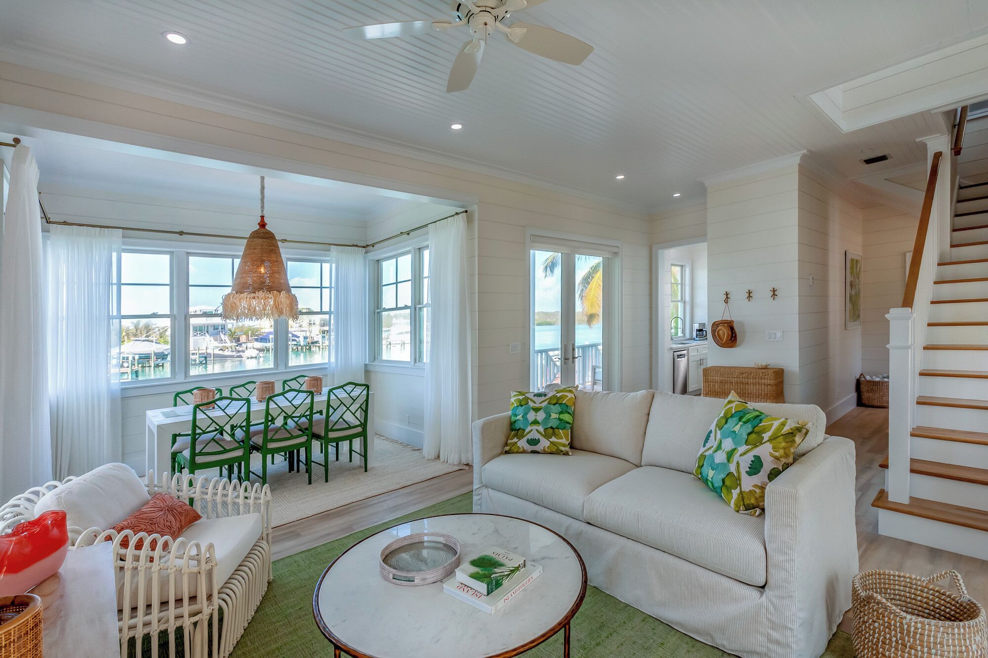 Un salón amplio con un sofá blanco, sillas verdes, una mesa de centro redonda y vistas al agua.