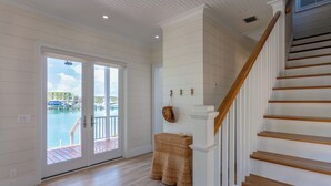 A spacious room with a wooden floor, a staircase with a wooden handrail, and a view of a marina through a sliding glass door. - 1 Bedroom Villa - Sunset Point, Abaco -SeaScape Villa # 9 (Elbow cay)
