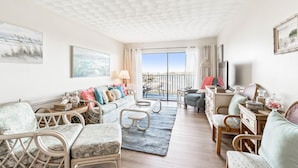 A spacious living room with a balcony, wicker furniture, and a view of the outdoors. - Charming Waterview Condo | 6 min wlk to beach! (Indian Shores)