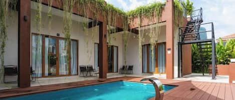 Une piscine avec une terrasse en bois, un espace salon extérieur et un coin abrité agrémenté de plantes.